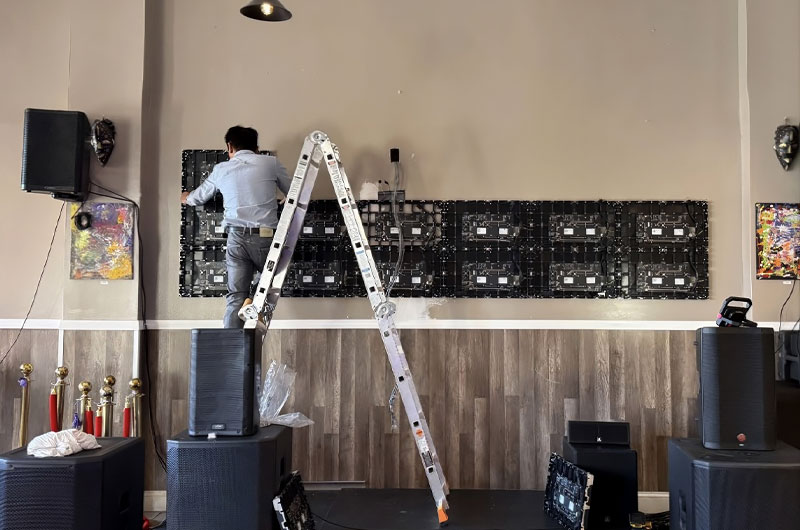 A technician on a ladder installing a DreamWall MicroLED video wall, showing the rear cabinet structure mid-installation