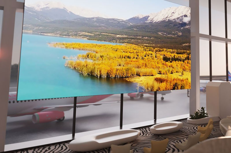 A large LED video wall displaying an aerial mountain and lake landscape in a modern airport lounge