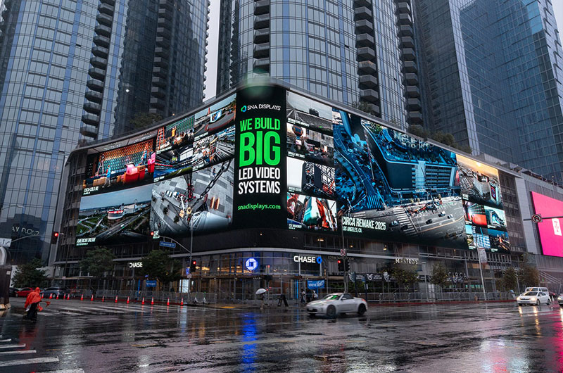 A large curved SNA Displays LED video system wrapping a city building reading We Build Big LED Video Systems